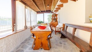 Una mesa de comedor de madera con sillas, un banco y una estantería en una habitación con suelo de piedra y vigas de madera en el techo.