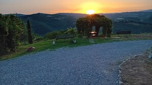 Un sendero de grava que lleva a un banco y un pabellón, con un atardecer de fondo.