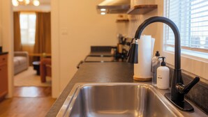 Una cocina moderna con un lavamanos de acero inoxidable, un grifo negro y una ventana con persianas.