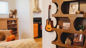 Una sala de estar con una guitarra, una estantería y una cocina al fondo.