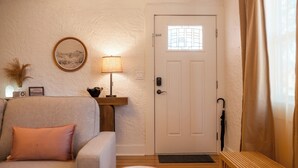 Una sala de estar con un sofá, una lámpara, una puerta y una ventana con cortinas.