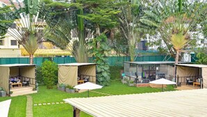 A courtyard with several covered seating areas, surrounded by lush greenery and palm trees. - King Suite with Balcony and Bathtub near UN Nairobi, Cozy Stead Garden House (Nairobi)