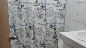 Kylpyhuone, jossa on meriaiheinen suihkuverho, wc ja pesuallas.
