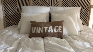 Sänky, jossa on valkoinen peitto ja tyyny, jossa lukee sana ”VINTAGE”.