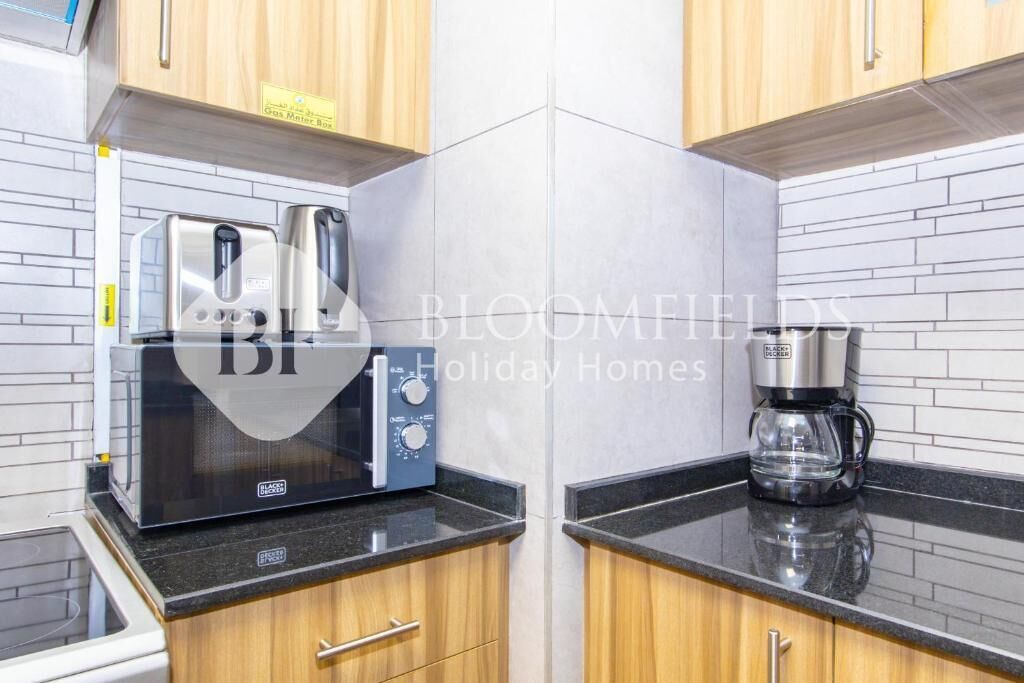 A kitchen with wooden cabinets, a microwave, a coffee maker, and a gas meter box.