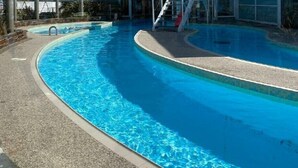 Ein Pool mit klarem, blauem Wasser, umgeben von einer Betonplattform und einem Glasgebäude im Hintergrund.