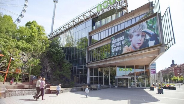 Un edificio moderno con una grande facciata vetrata, una ruota panoramica sullo sfondo e un cartellone pubblicitario per uno spettacolo per bambini.
