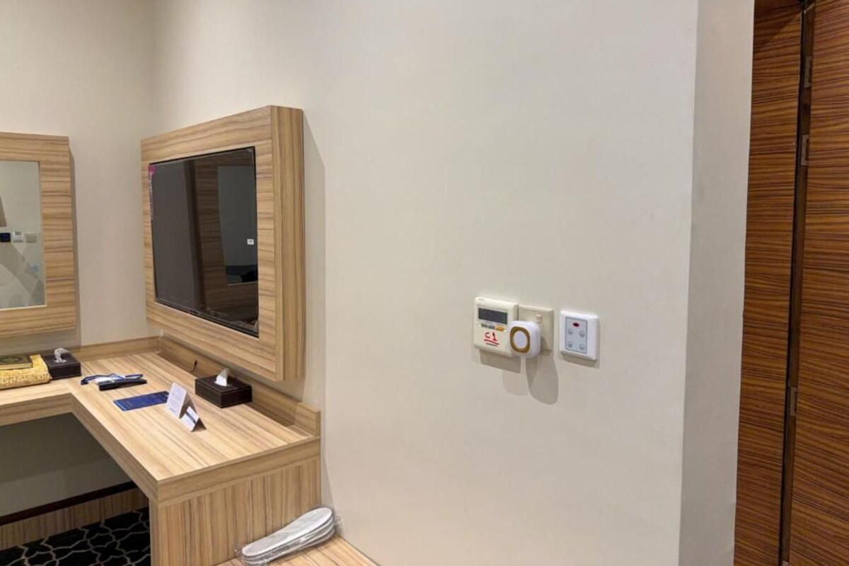 Habitació d'hotel amb escriptori de fusta, televisió de pantalla plana, termòstat fixat a la paret i armari de fusta.