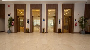 Una hall con pavimento in piastrelle lucide, pannelli in legno e una serie di porte che conducono a diverse aree.