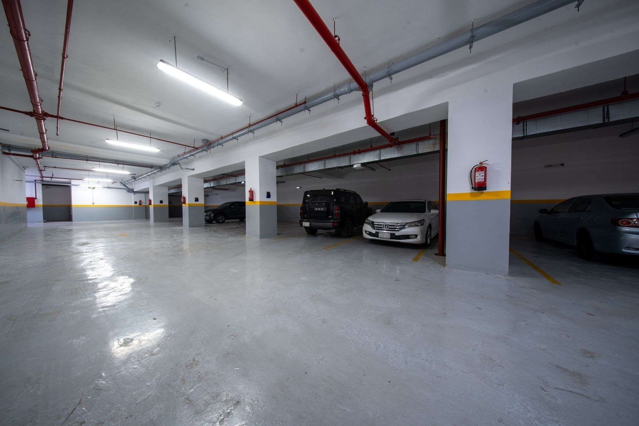 Un parcheggio multipiano con pavimenti in cemento, pareti bianche e tubature rosse.