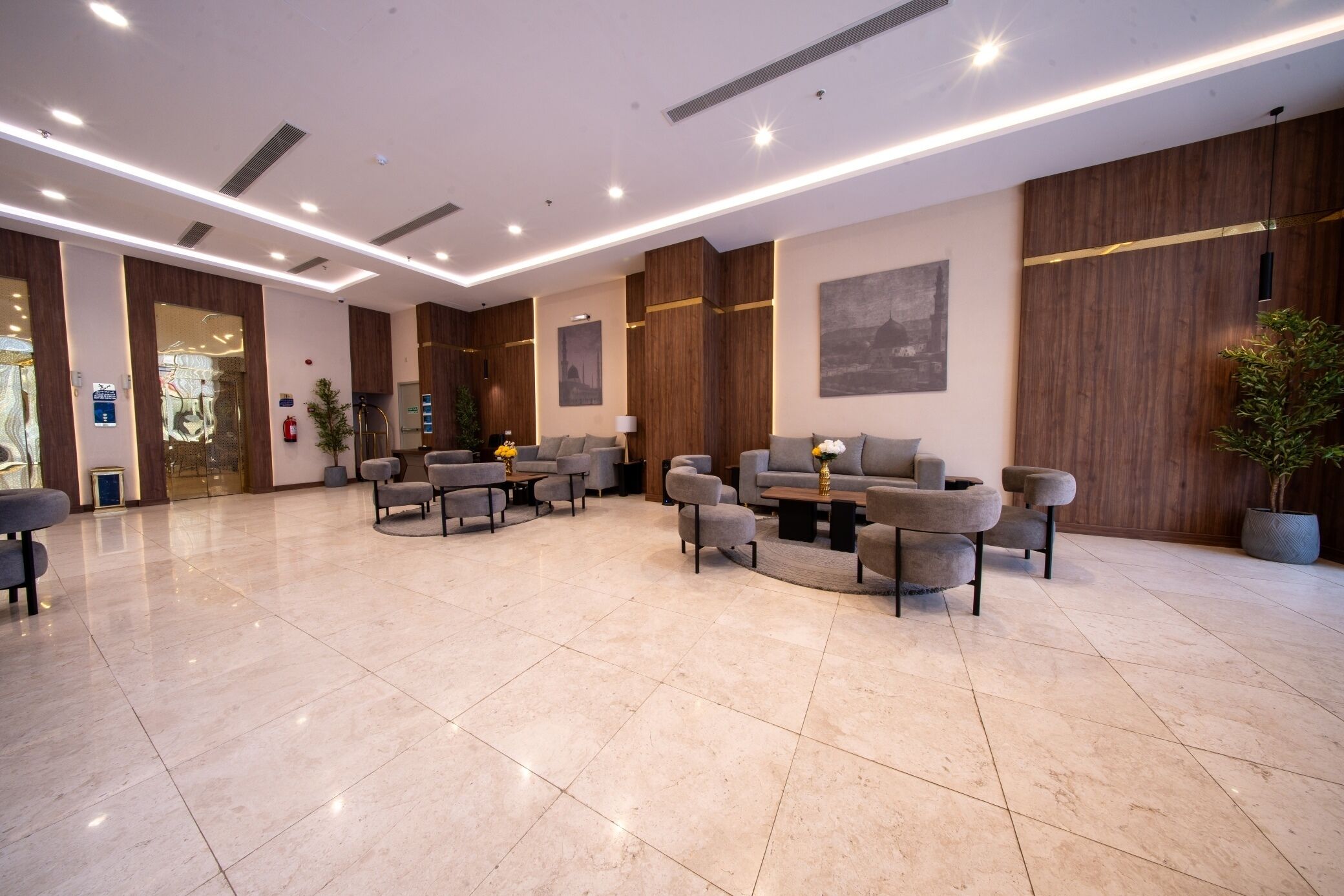 A spacious lobby with a modern design, featuring a seating area with sofas and armchairs, a reception desk, and a large wall-mounted painting.