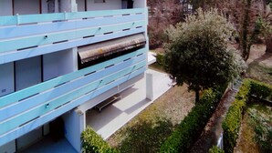 Un edificio moderno con techo plano y una serie de ventanas. Cuenta con un jardín bien cuidado, con arbustos variados y un árbol.