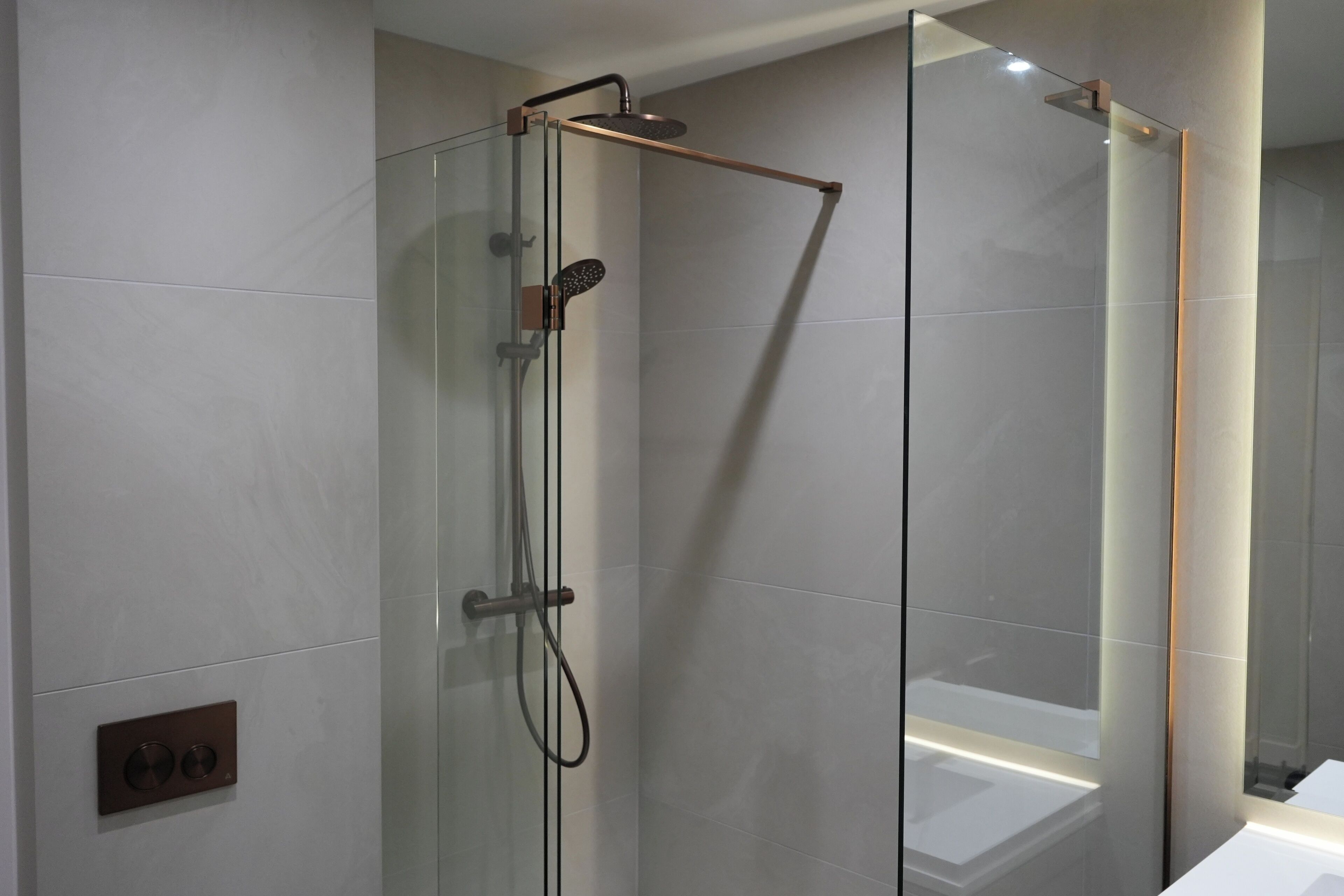 A modern shower with a glass enclosure, a handheld showerhead, and a wall-mounted control panel.