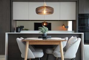 Uma cozinha moderna com ilha central, duas cadeiras estofadas cinzas, uma mesa de madeira e uma luminária pendente.