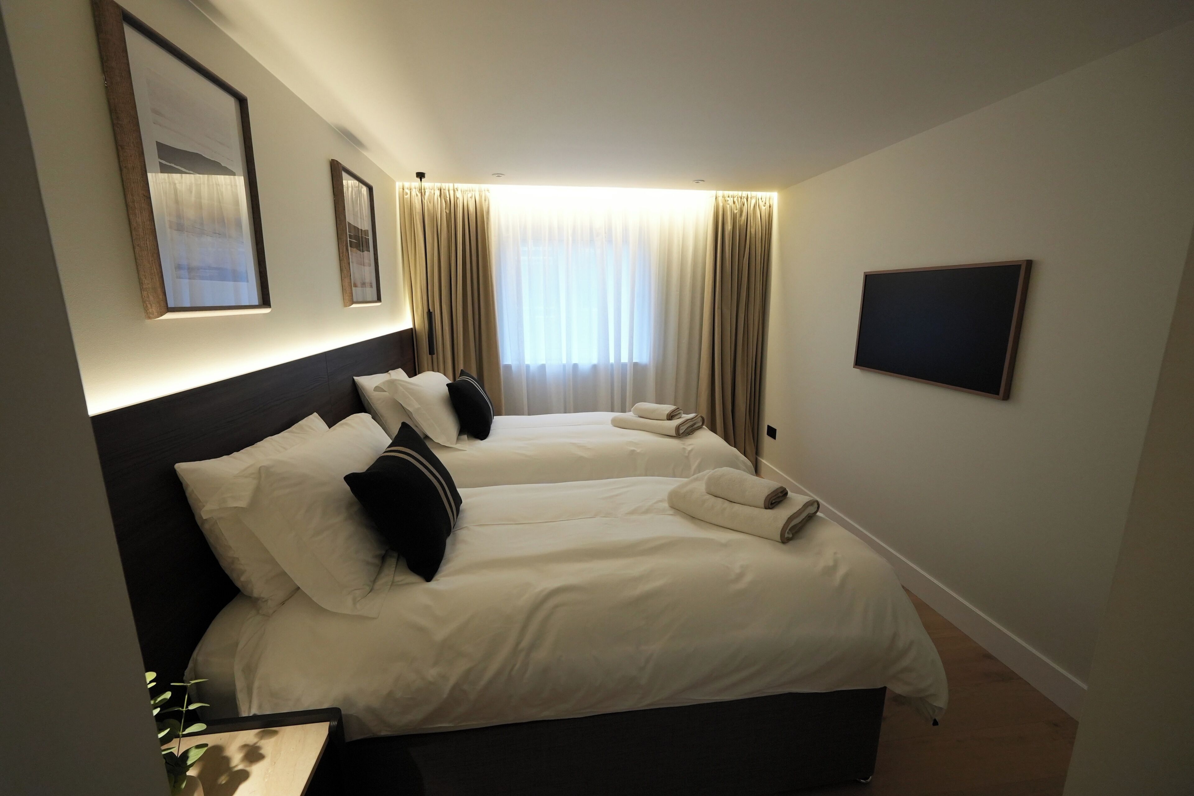 Une chambre d’hôtel avec deux lits, un téléviseur à écran plat et une grande fenêtre avec des rideaux.