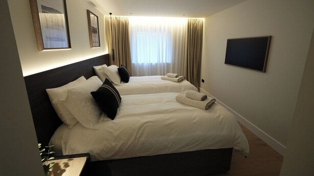 A hotel room with two beds, a flat-screen TV, and a large window with curtains. - 1st Floor Luxury 2-bed Apt, Sleeps 6 (St. Andrews)