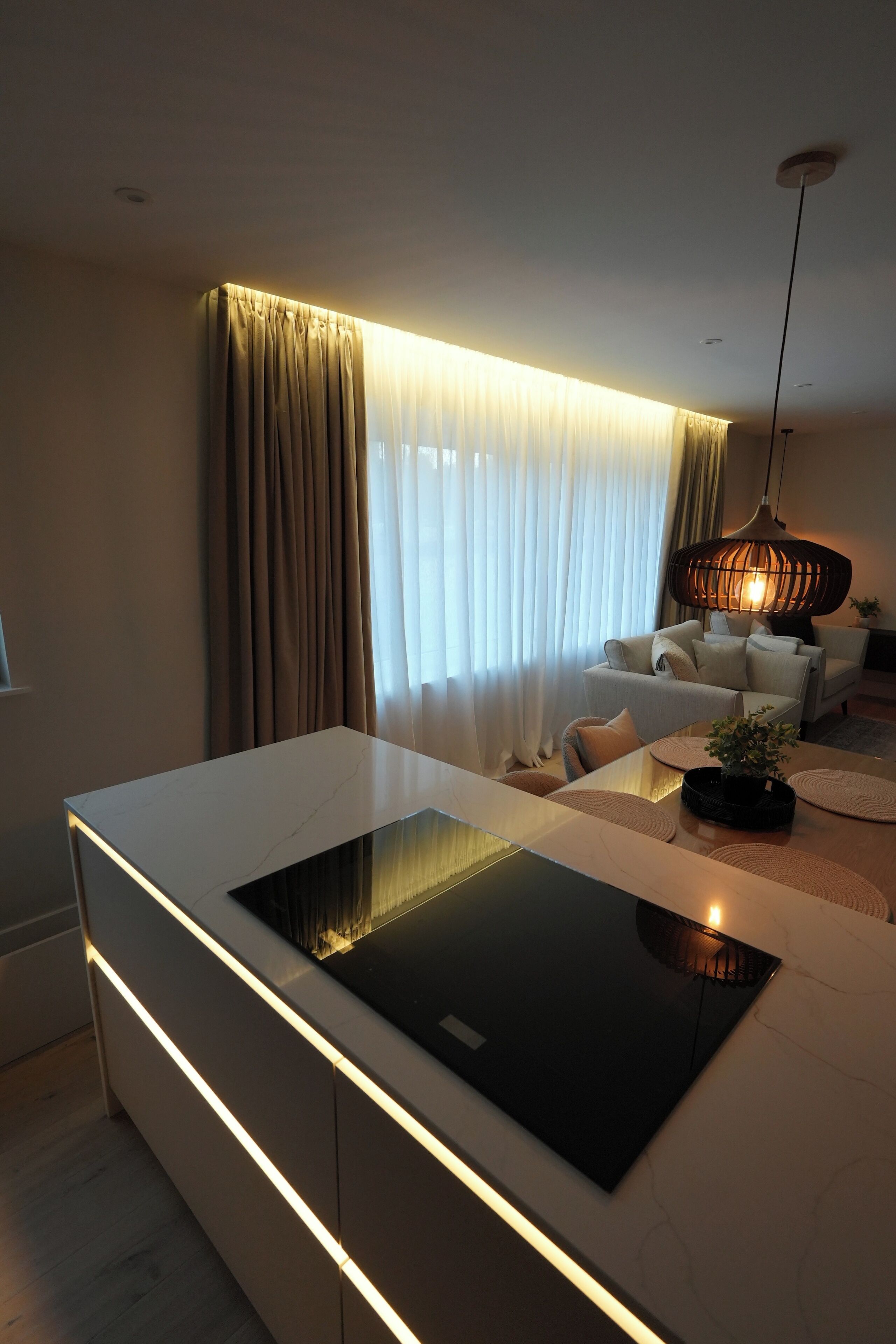 Ein modernes Wohnzimmer mit einem eleganten weißen Sofa, einer Kücheninsel mit Glasplatte und einer hängenden Leuchte.