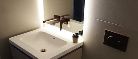 A bathroom with a white sink, a mirror, a toilet, and a light fixture.