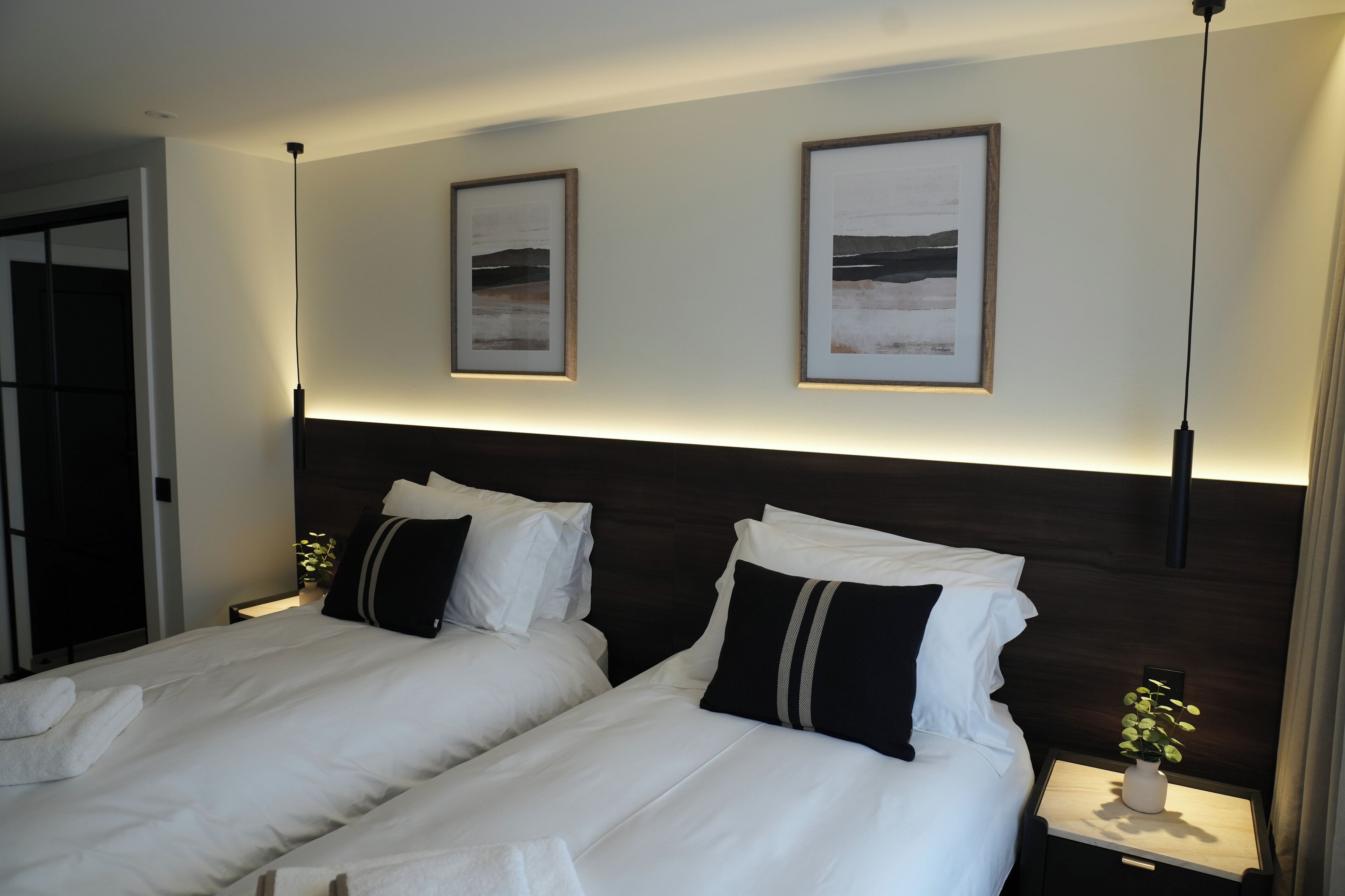 Een hotelkamer met twee bedden, een kunstwerk aan de muur, nachtkastjes met lampen en een deur links.