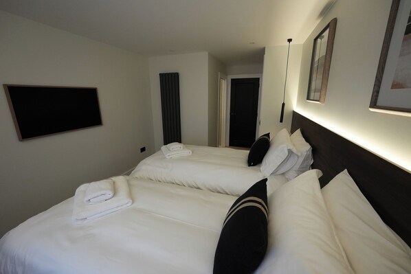 A hotel room with two beds, a flat-screen TV mounted on the wall, and a framed picture above the beds. - 1st Floor Luxury 2-bed Apt, Sleeps 6 (St. Andrews)