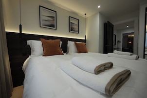 Quarto de hotel com uma cama grande, duas almofadas, uma cabeceira e duas imagens emolduradas na parede.