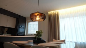 A modern dining area with a central table, chairs, a hanging light fixture, a potted plant, and a window with curtains. - 1st Floor Luxury 2-bed Apt, Sleeps 6 (St. Andrews)