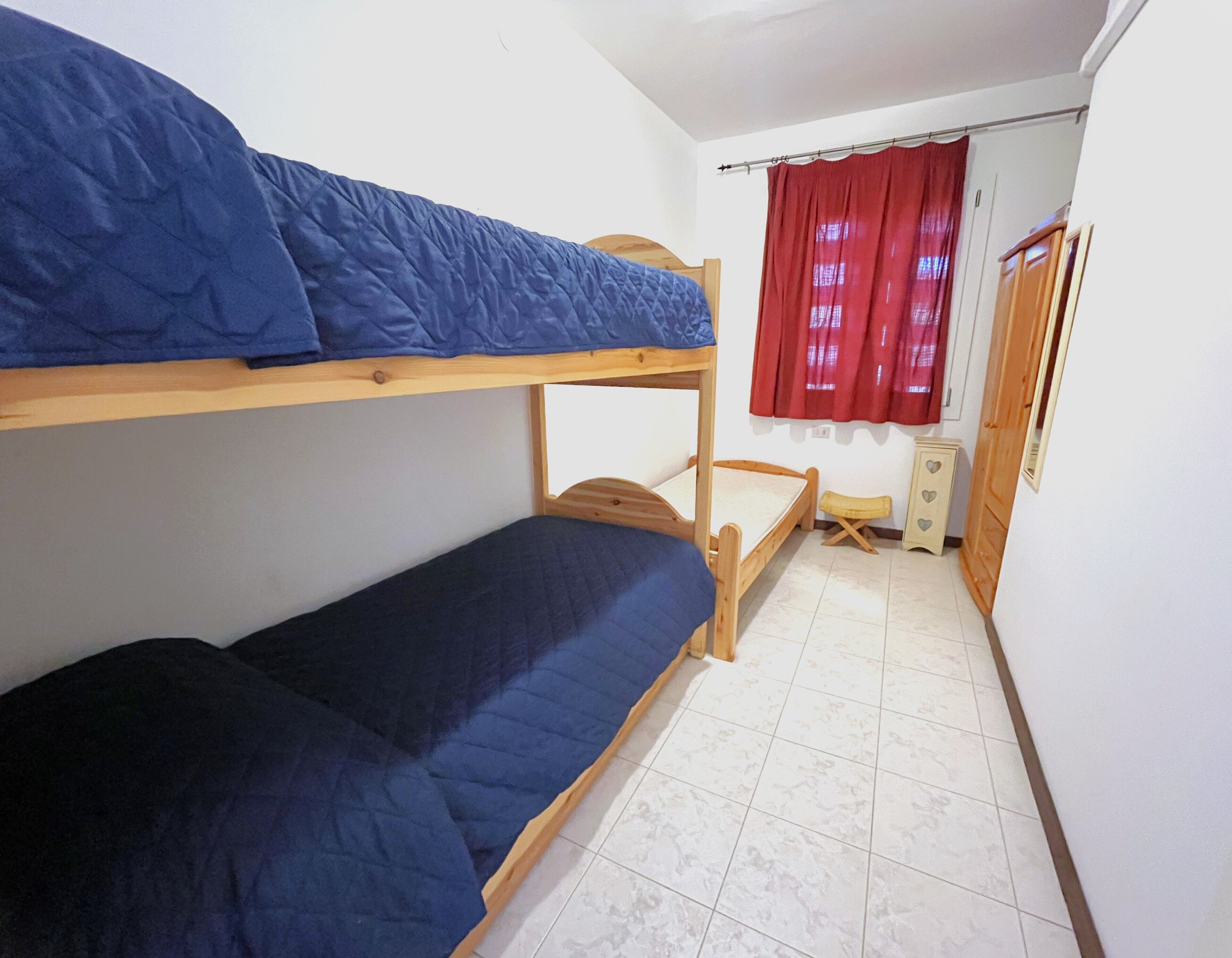 Habitación con literas, cabecera de madera, un taburete pequeño y un armario con adornos de corazón.