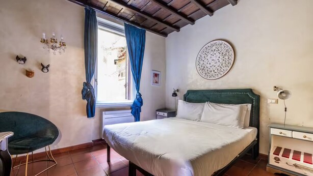 A bedroom with a bed, a chair, a desk, a chandelier, and a decorative wall piece. - Welcome in charming loft in Campo dè Fiori (Roma)
