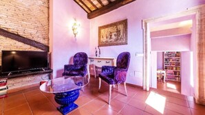 A living room with a fireplace, two purple armchairs, a glass coffee table, and a bookshelf. - Welcome in charming loft in Campo dè Fiori (Roma)