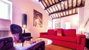 A living room with a red sofa, patterned armchairs, a glass coffee table, and a fireplace. - Welcome in charming loft in Campo dè Fiori (Roma)