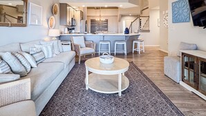 A spacious living room with a large sofa, a coffee table, and a kitchen area in the background. - Heavenly Pointe | Penthouse Lake Views, Elevator, Accessible, King Beds (Branson)