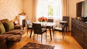 A living room with a wooden ceiling, a dining table with chairs, a sofa, a TV, and a fireplace. - Village house in a quiet location, green oasis vacation home (Hefersweiler)