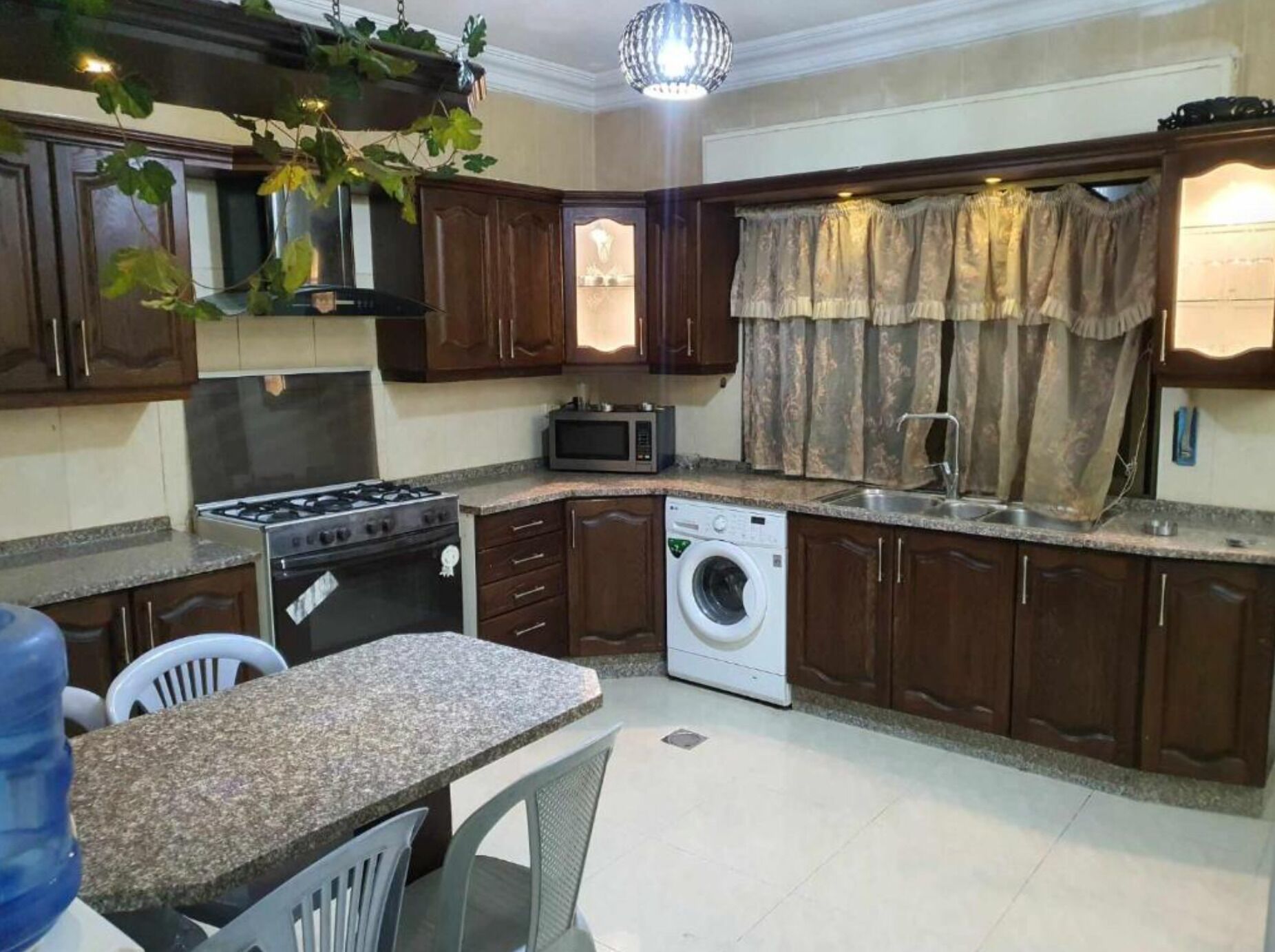 A compact kitchen with a gas stove, microwave, and washing machine. There is a dining area with chairs and a table.