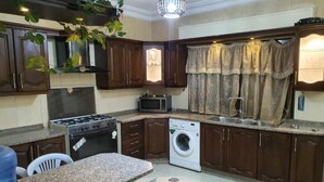 Cozinha compacta com fogão a gás, micro-ondas e máquina de lavar. Há um espaço de refeições com cadeiras e mesa.