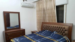 Quarto com cama, penteadeira, espelho, ar condicionado e janela com cortinas.