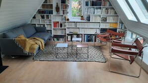 Un racó acollidor per llegir amb un sofà gris, una manta marró, una taula petita i una prestatgeria plena de llibres.
