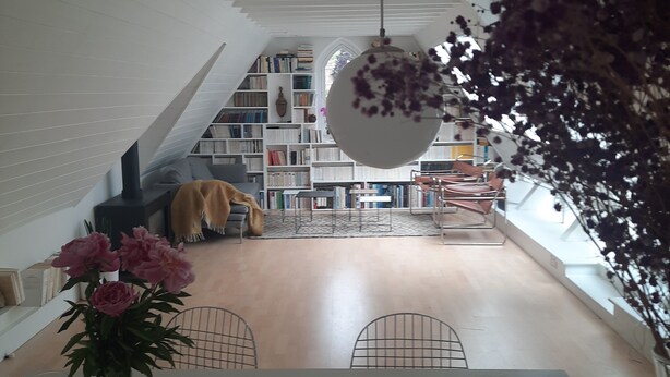 Un interior modern amb una escala que condueix a una zona estalviada, una gran biblioteca i un llum penjant.