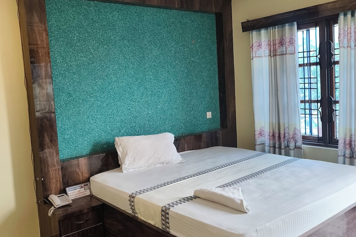 A hotel room with a large bed, a ceiling fan, a telephone on a bedside table, and a window with curtains.
