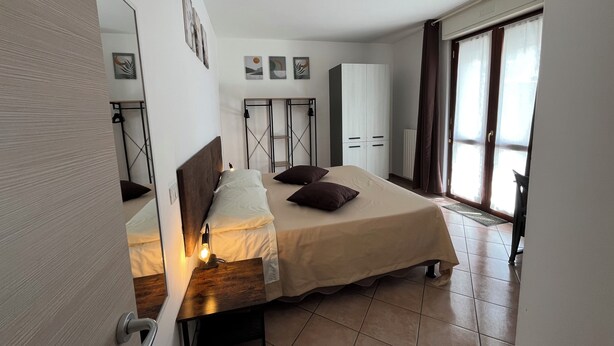 Une chambre à coucher comprenant un lit, une table de chevet, une lampe, une armoire et donnant sur l’extérieur.