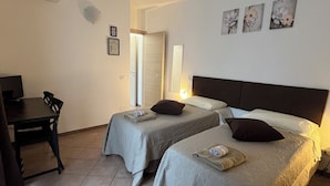 Une chambre d’hôtel avec deux lits, un bureau et une chaise. Des lampes sont fixées au mur, et une porte donne accès à une autre pièce.