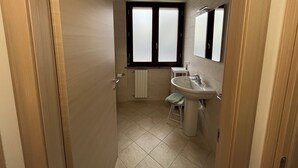 Un couloir étroit mène à une salle de bain équipée d’une fenêtre, d’un lavabo et d’un porte-serviettes.