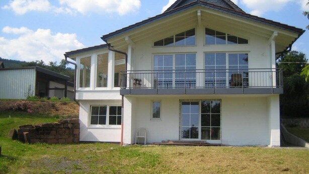 Et toetagers hus med balkon, store vinduer og en stenvæg foran.