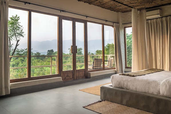 A bedroom with a large window, a bed, and a view of greenery. - Utsav Camp Sariska (Rajgarh)