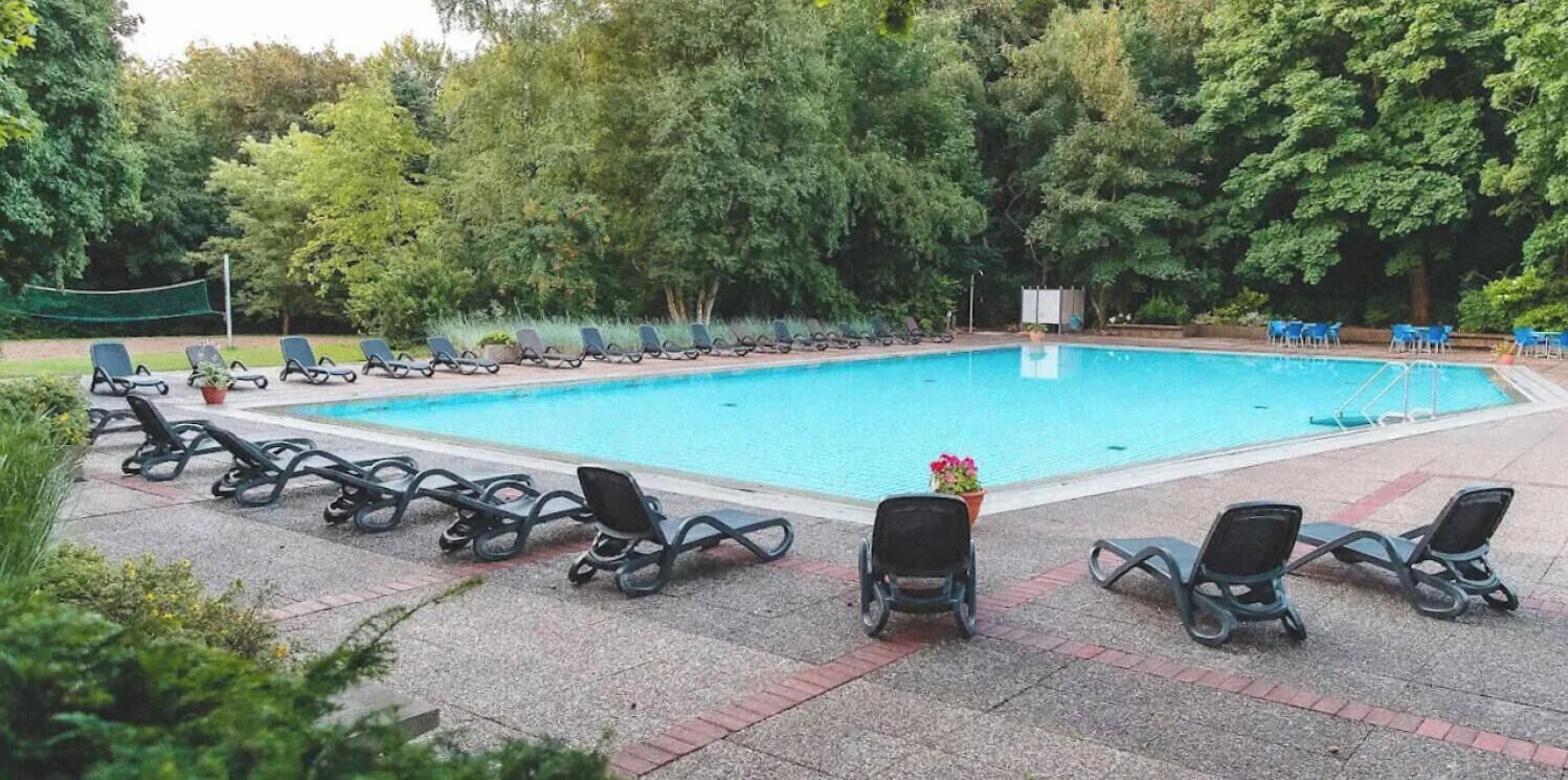 Una piscina con sillones de descanso alrededor, rodeada de árboles.