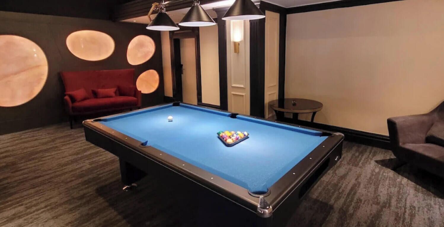 Una mesa de billar con un sofá rojo y una pequeña mesa redonda en una habitación con paredes y luces de techo oscuras.