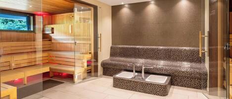 A modern sauna with wooden benches and a glass partition, a seating area with a patterned bench, and a tiled wall.
