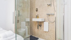 Un baño moderno con cabina de ducha de vidrio, un lavamanos blanco y un inodoro.