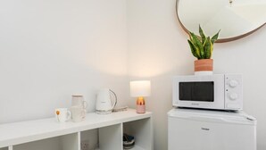Una kitchenette blanca con microondas, hervidor y una pequeña mesa con tazas y una planta.