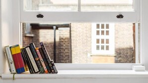 Un alféizar con una hilera de libros y vista a un edificio de ladrillo a través de la ventana.