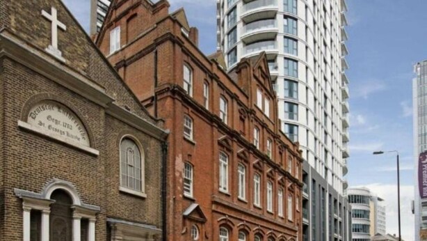 Un edificio histórico con una cruz en la fachada, junto a un moderno rascacielos.
